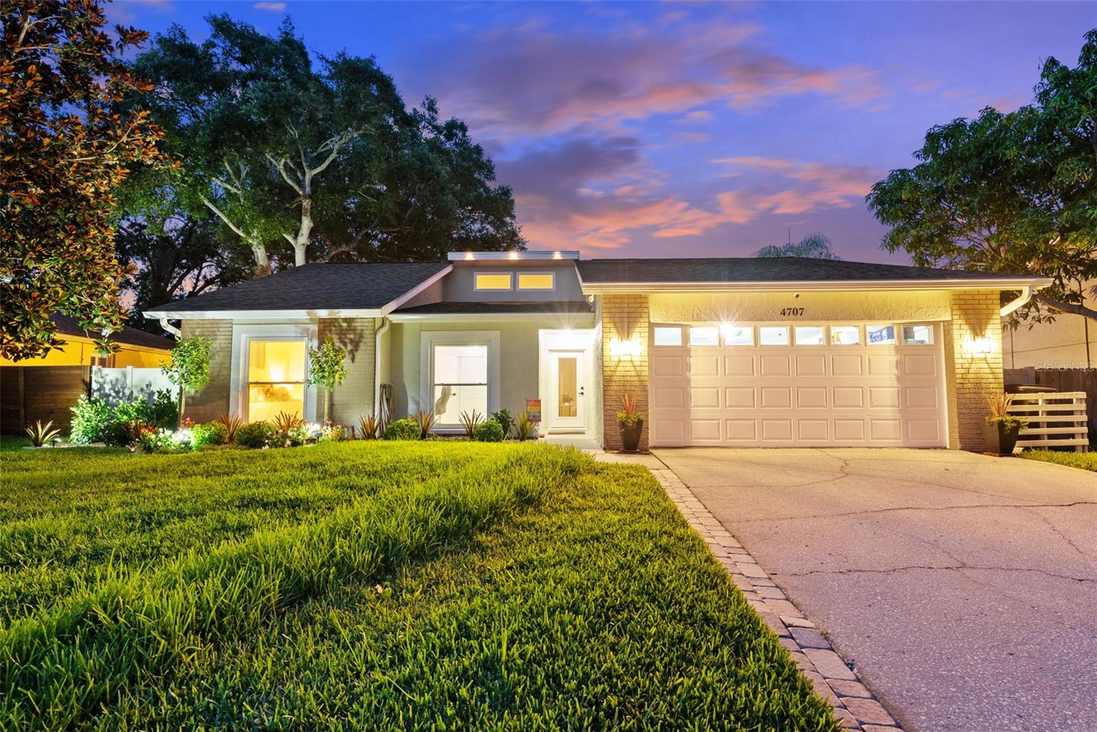 Additional front facing nighttime shot with lighting on exterior of home fence and trees.