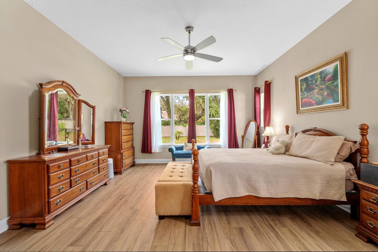 The really spacious primary bedroom features high-end LVP floors, 2 large walk-in closets, a lighted ceiling fan with remote, and 3 windows for natural light and pretty views.