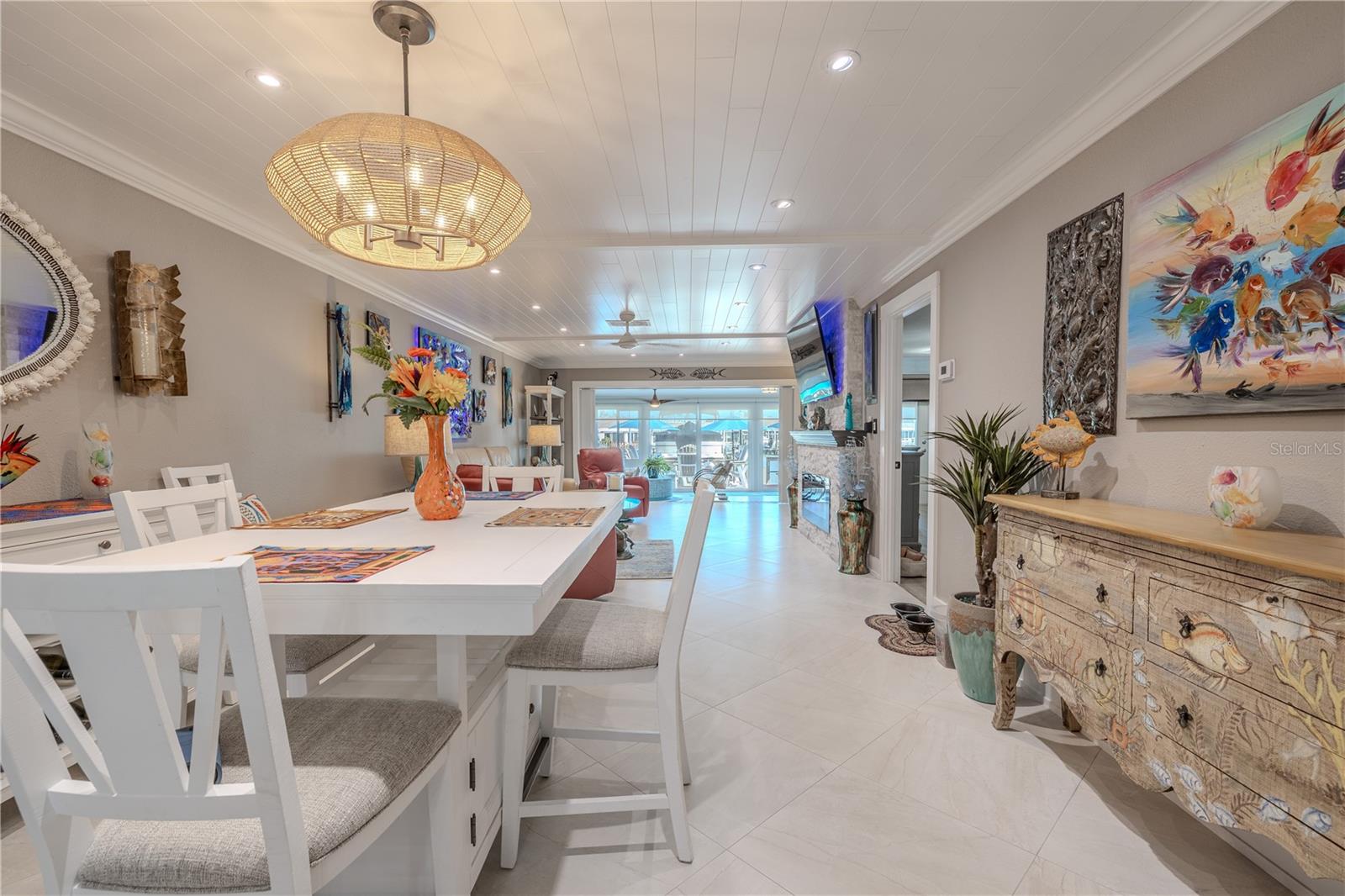 Open-concept living space featuring shiplap ceilings with recessed LED lighting, large-format tile flooring laid on the diagonal, and expansive sliding glass doors that frame serene waterfront views. Clean architectural lines and neutral finishes create a bright, seamless flow from the dining area to the main living space.