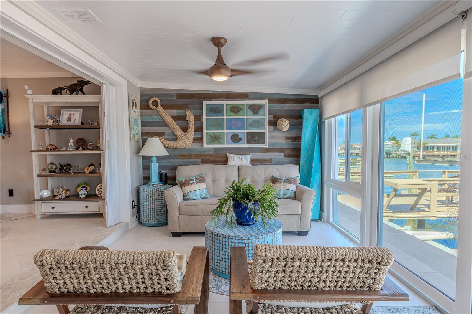 This bright and inviting Florida room features a rustic barn-style accent wall that adds texture and character to the space. Expansive hurricane-rated impact sliding glass doors and windows—tested to withstand up to 185 mph winds—offer peace of mind along with panoramic waterfront views.