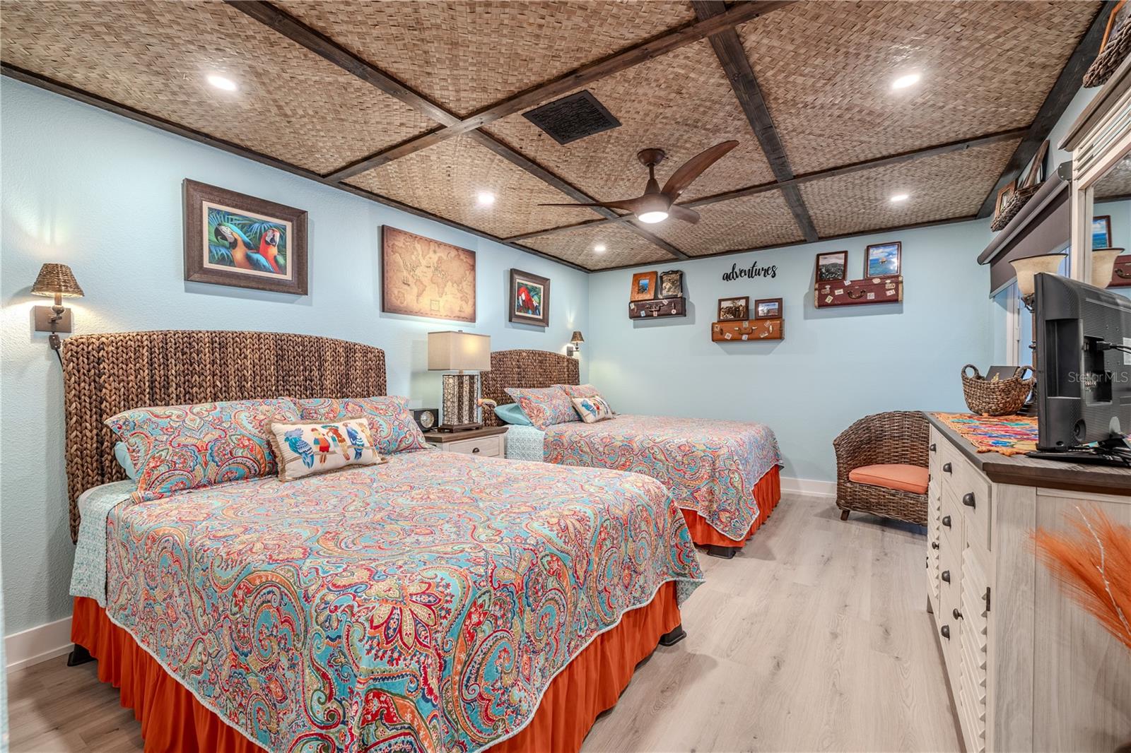 This generously sized guest bedroom features high-end waterproof plank flooring and ample space to accommodate multiple beds with room to spare. The custom ceiling is a showstopper—crafted with authentic matting imported from Hawaii, it brings a distinct tropical aesthetic that sets the room apart. A Minka ceiling fan in Kona wood finish adds both function and flair, perfectly complementing the island-inspired ceiling. Recessed lighting provides a clean, modern finish to this thoughtfully designed space.