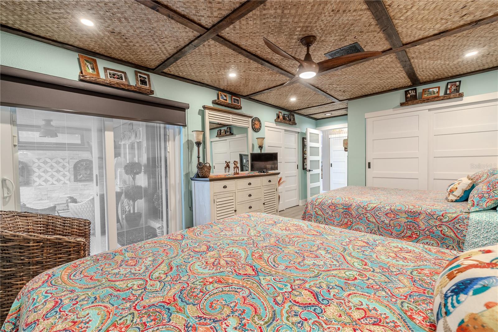 This angle of the guest room highlights the glass sliding doors with built-in blinds that open directly to the front lanai, bringing in natural light while preserving privacy. A roll-down blackout shade offers added comfort for midday naps or late risers. Two generously sized closets with 5-panel bypass doors (one 5 feet wide, the other 6 feet) provide an abundance of practical storage without sacrificing style.