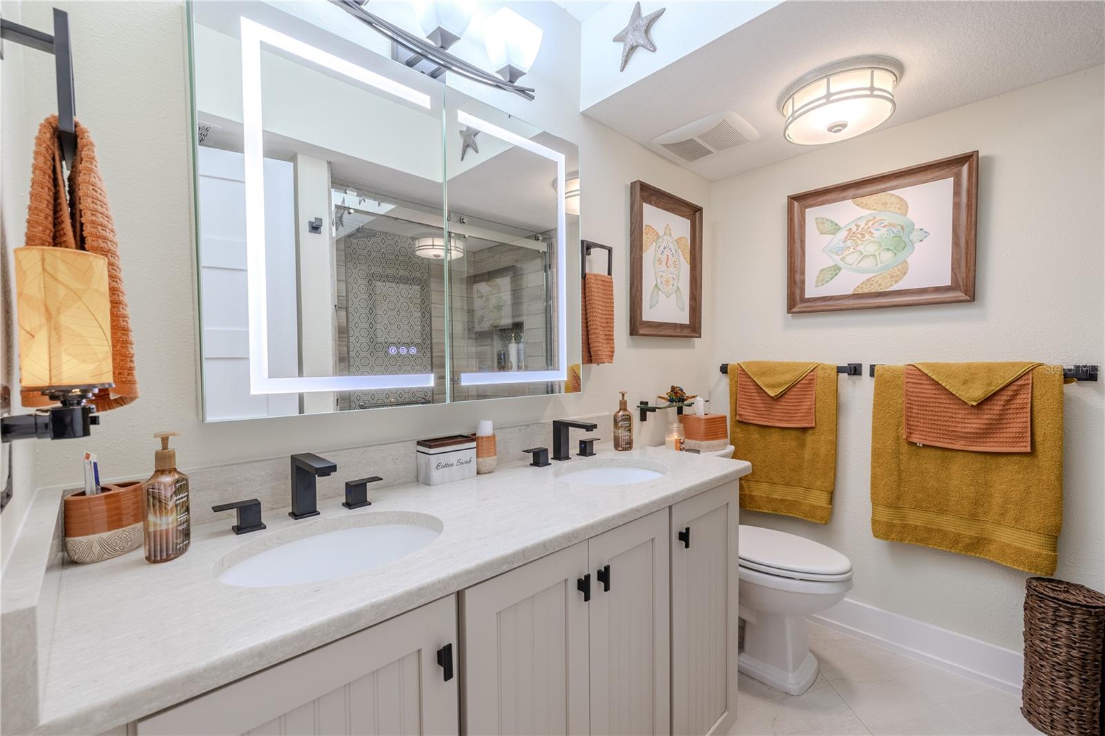 The guest bath features a quartz countertop with double sinks and sleek matte black fixtures. A high-efficiency dual-flush toilet adds function without sacrificing form. The real standout? A smart LED medicine cabinet with integrated lighting on both the interior and exterior, adjustable to three different light temperatures—and yes, it even has a built-in defogger for a crystal-clear mirror, every time.