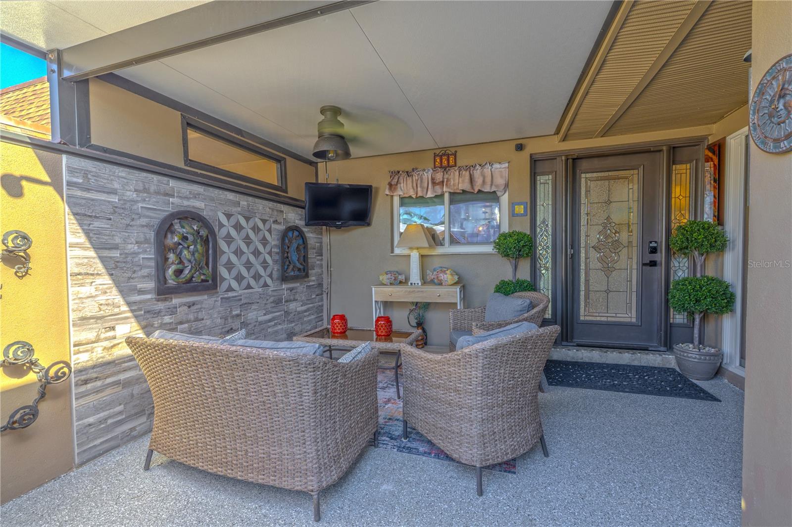 The front lanai is equal parts function and style—featuring a lifetime-warrantied epoxy floor, two custom architectural tile feature walls, and a built-in TV with ceiling fan for year-round comfort. The inviting sitting area is the perfect spot to unwind or entertain, with a direct view of the beautifully detailed front entry door. A retractable screen allows fresh air to breeze through the home from front to back when the rear sliders are open, creating natural cross-ventilation and a true indoor-outdoor connection.