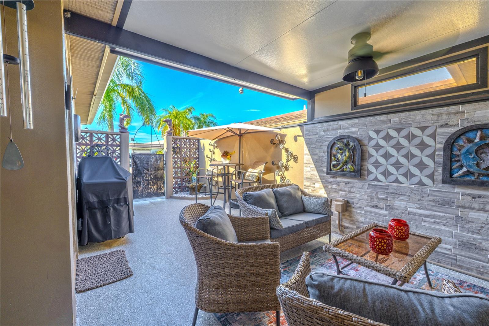 A welcoming covered front lanai/patio brings the outside-in with a transom window, new epoxy surface floor with a lifetime warranty, two custom tile feature walls, sitting area, TV, and ceiling fan.