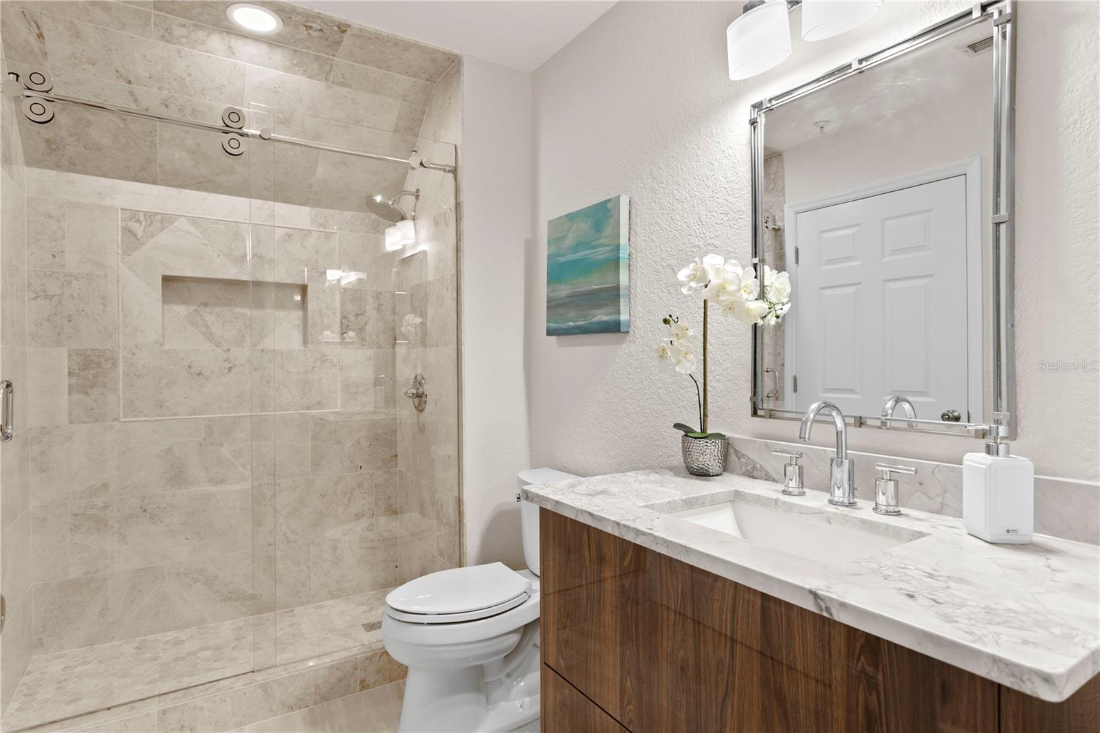 Modern cabinetry extends into the bathroom for a unified aesthetic, while the shower features built-in shelving for added function and style.