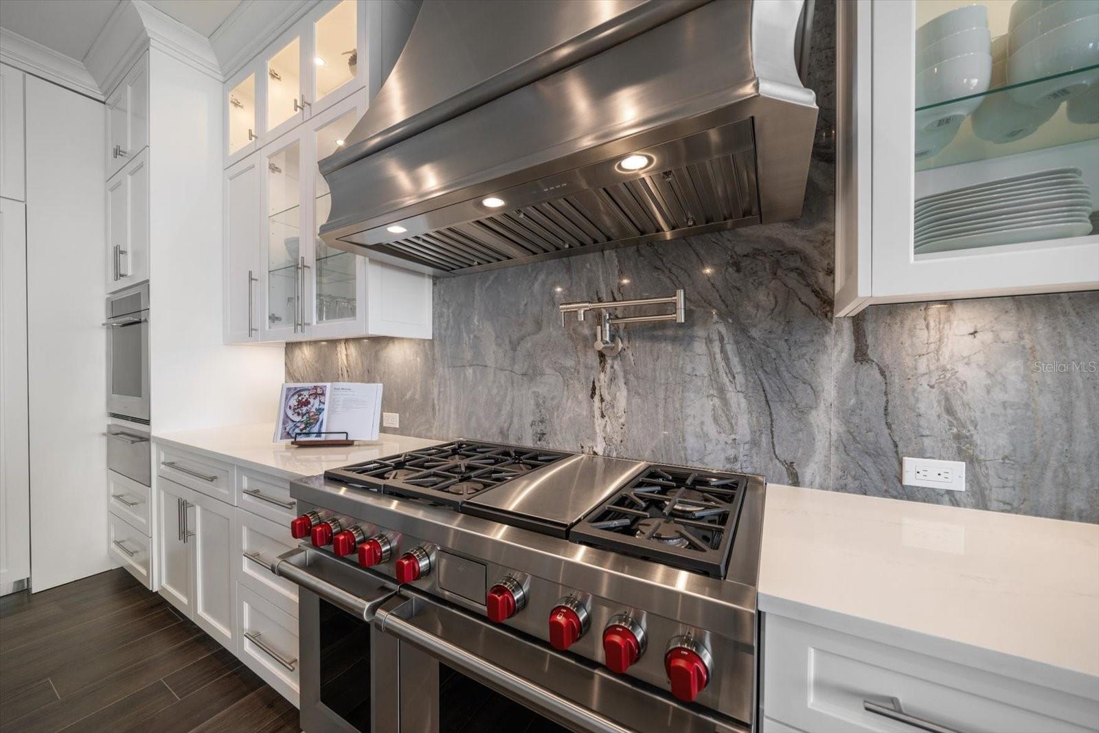 Wolfe gas stove, pot filler faucet, and stainless ventilated hood accented by natural stone backsplash.