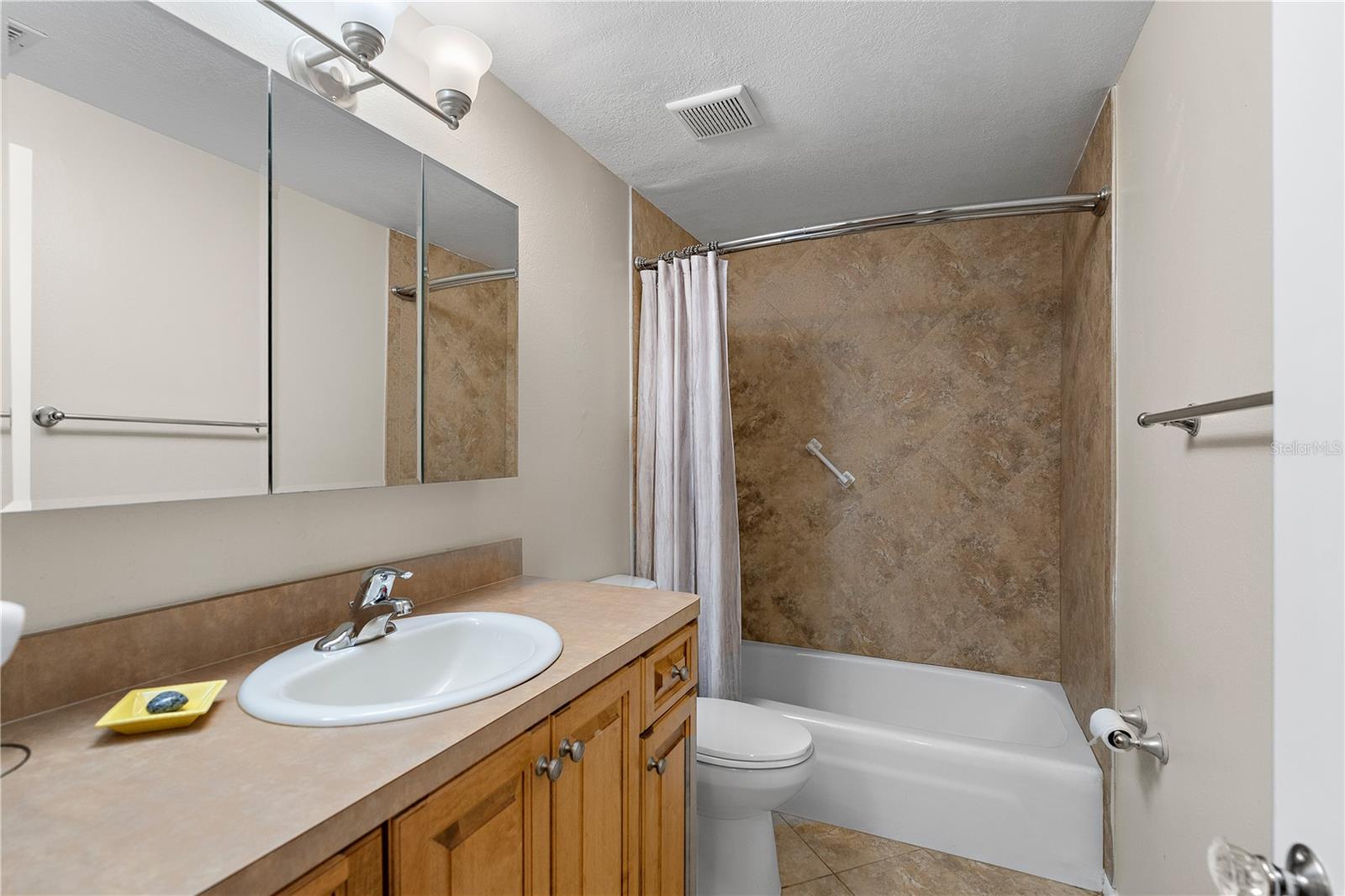 The second bathroom has wood cabinets, neutral tile and a tub/shower combination.