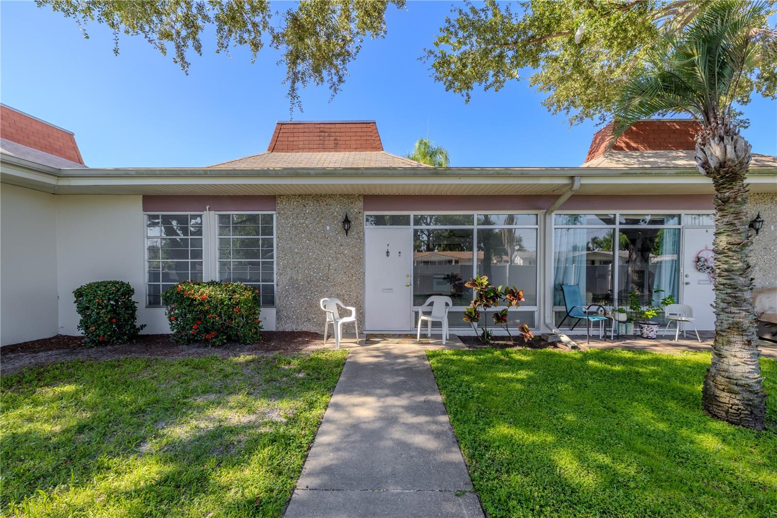 Welcome to your charming Florida retreat in the desirable 55+ community of Tahitian Gardens! This well-maintained 2-bedroom, 1-bath condo offers a clean and inviting exterior with a welcoming front patio perfect for enjoying your morning coffee or evening breeze. A paved walkway leads to the front entrance, flanked by mature shrubs and lush green lawn, offering just the right touch of privacy and curb appeal.