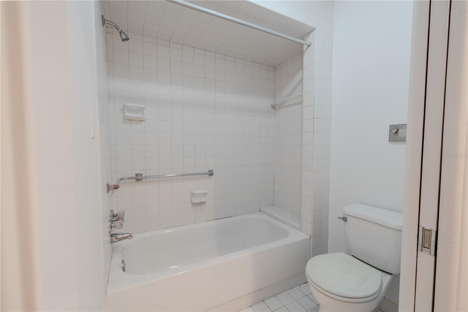 a tub-shower combo with classic square tiles offers versatility and convenience. Dual towel bars and thoughtful lighting above the mirror make this a functional space that’s ready for your personal updates or mid-century modern revival. Whether you're starting fresh or looking to modernize, this bathroom provides a solid foundation with generous space and vintage charm.