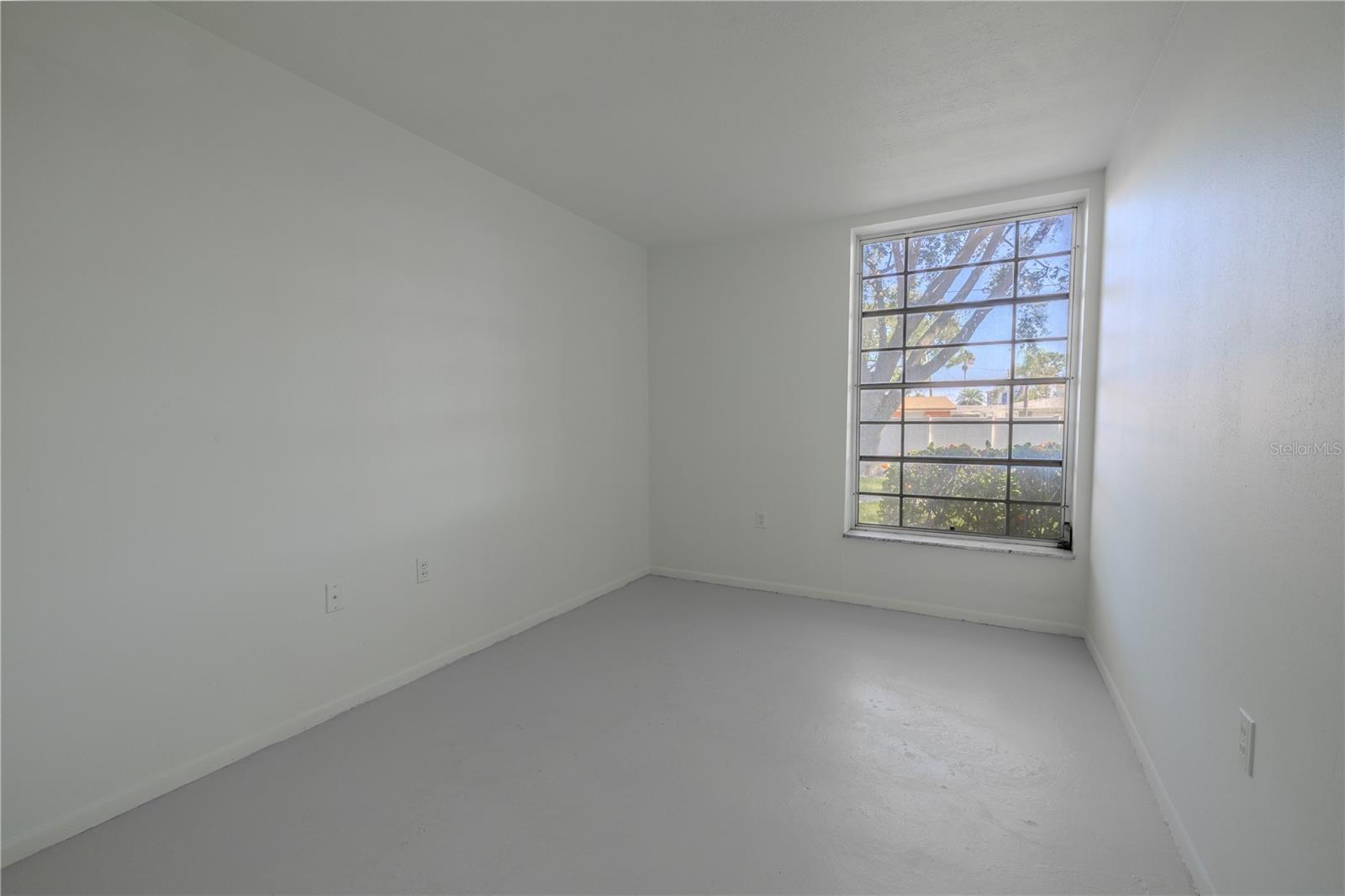 Bedroom 2 offers a bright and inviting space, ideal for guests, a home office, or a cozy personal retreat. A large window fills the room with natural light and offers a pleasant view of the landscaped courtyard outside.