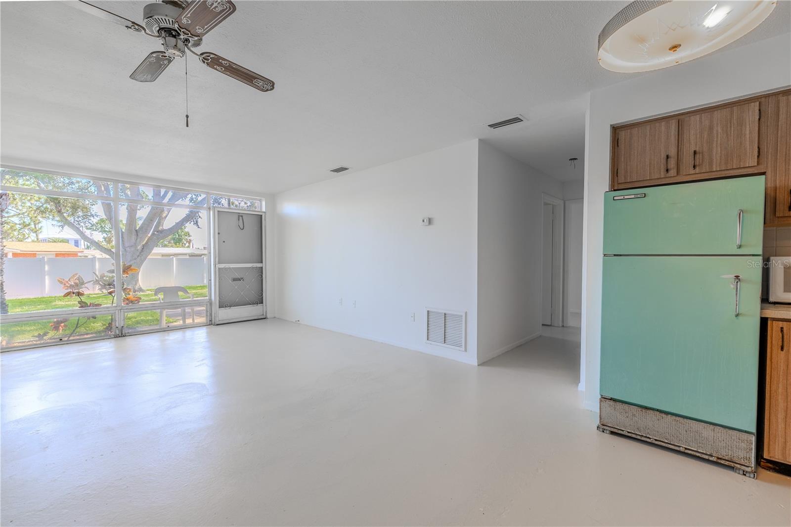 The spacious dining and living area is bright, airy, and filled with natural light thanks to a full wall of oversized windows overlooking the lush green courtyard. A neutral color palette, freshly painted walls, and clean flooring create a blank slate ready for your personal touch.