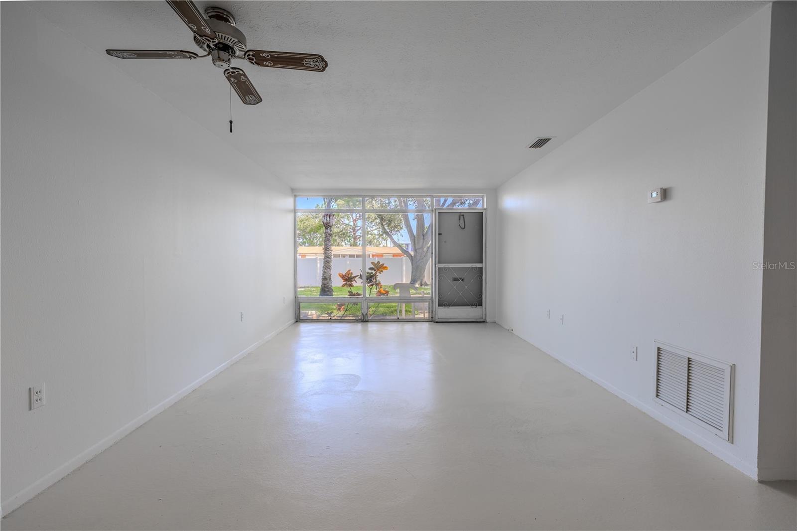 his light-filled dining and living area offers a spacious, flexible layout perfect for customizing to your lifestyle. Freshly painted in crisp white with matching neutral floors, the space feels clean, open, and modern. A wall of floor-to-ceiling windows welcomes in abundant natural light and frames a peaceful view of the landscaped green space just outside your front door.