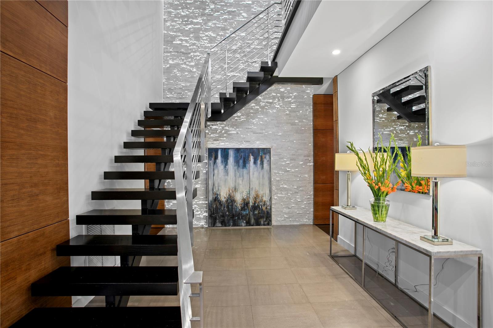 Beyond the front door lies an artfully designed foyer, anchored by a bold floating staircase that seamlessly blends industrial strength and organic beauty