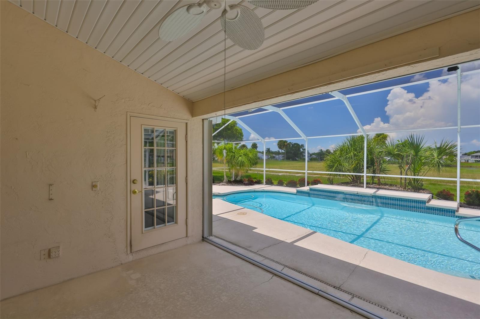 Covered lanai looking to screened lanai. Ceiling fan, pool doors with built-in blinds, sliders to Great Room behind.