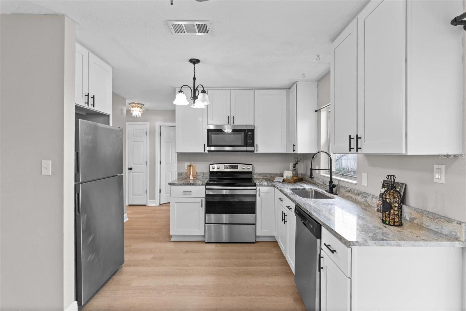 Updated kitchen featuring white shaker cabinets, granite counters, and stainless steel appliances.