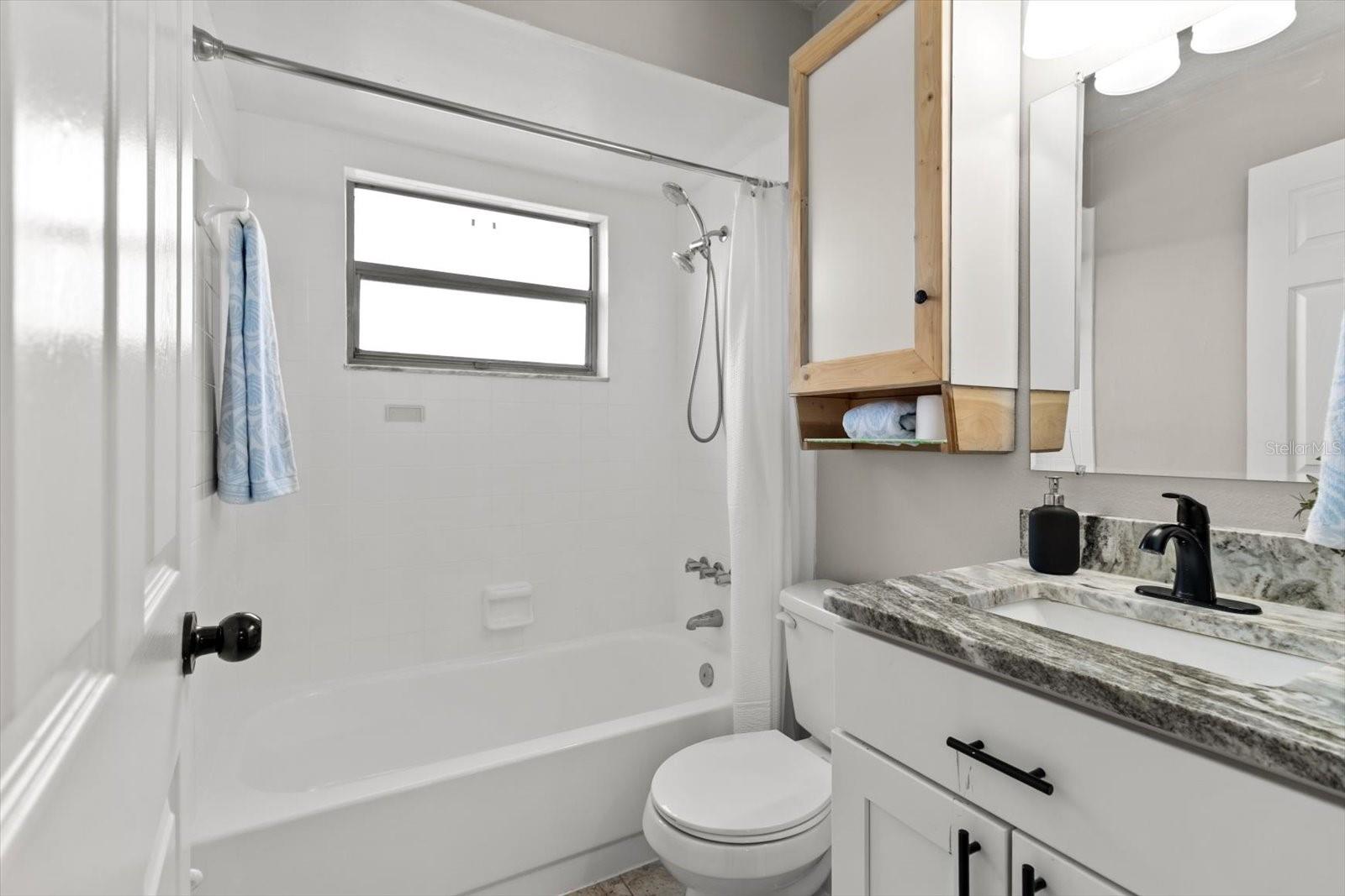 Modern vanity, granite countertop, and a clean tub-shower combo with natural light.