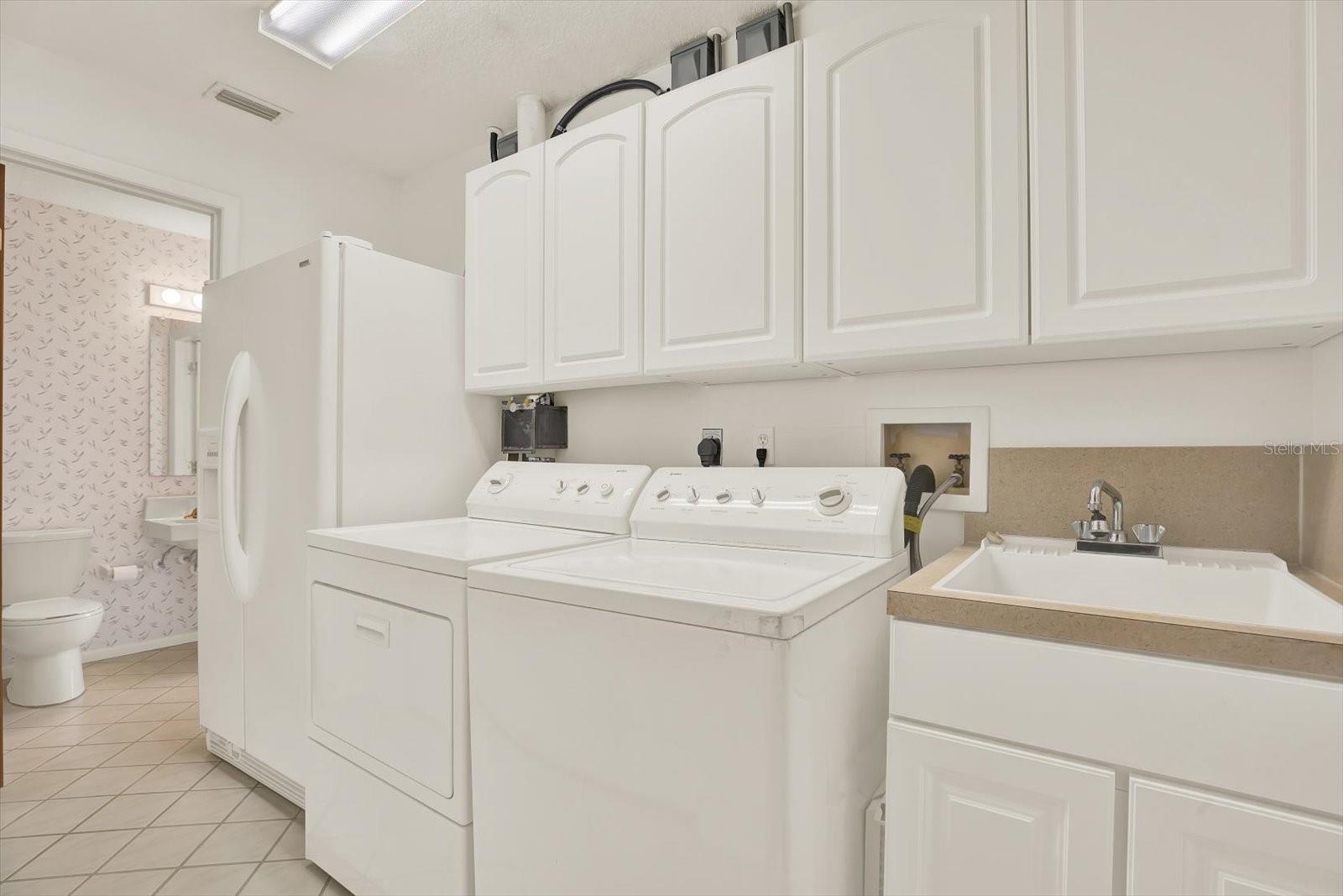 Laundry room with wash sink and second refrigerator.  Half bath connecting to the Bonus room in the background.