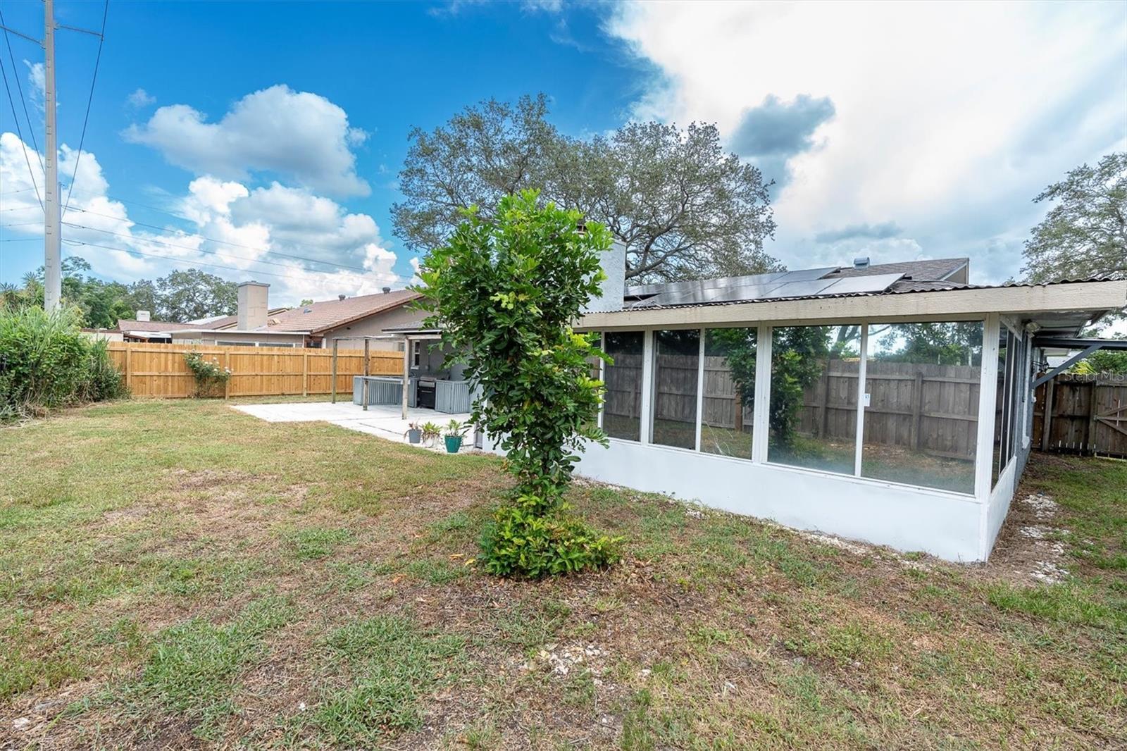 View of fenced back yard, sunroom and patio