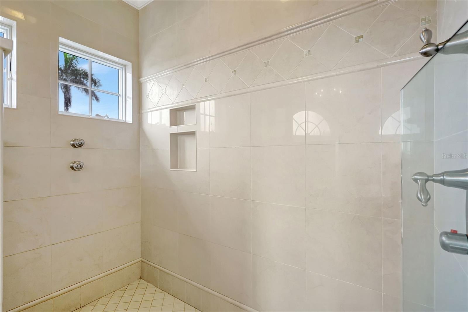 The walk in primary bathroom shower features glass doors, lovely tile, niches & water views!