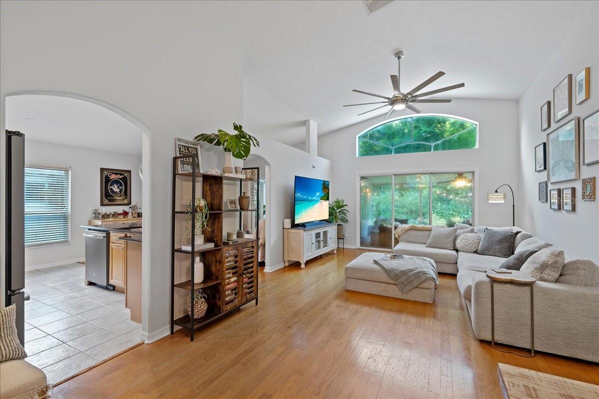 Spacious living room with triple glass sliders, decorative transom window, vaulted ceilings, ceiling fan and beautiful oak flooring