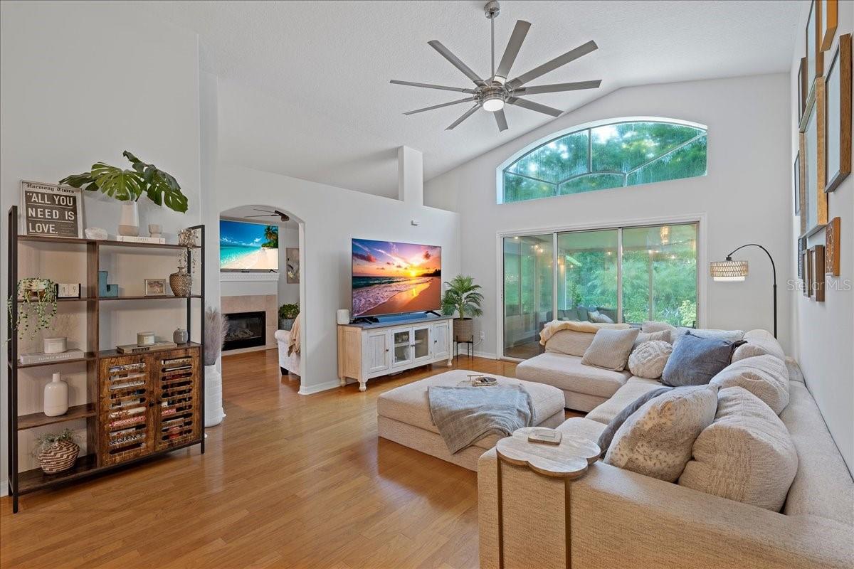 Spacious living room with triple glass sliders, decorative transom window, vaulted ceilings, ceiling fan and beautiful oak flooring
