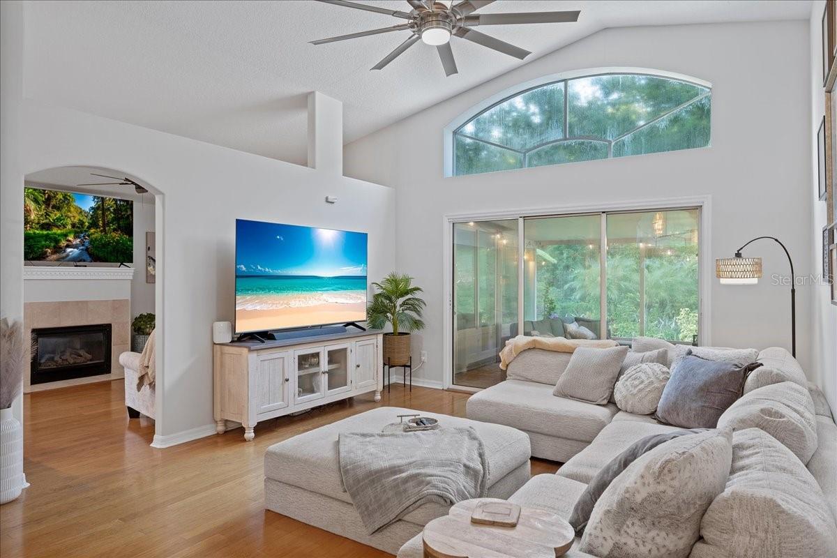 Spacious living room with triple glass sliders, decorative transom window, vaulted ceilings, ceiling fan and beautiful oak flooring