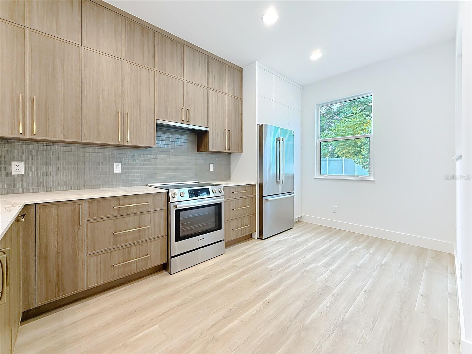 Sleek and modern kitchen featuring custom wood cabinetry, quartz waterfall countertops, stainless steel appliances, and stylish accent details — all bathed in natural light.