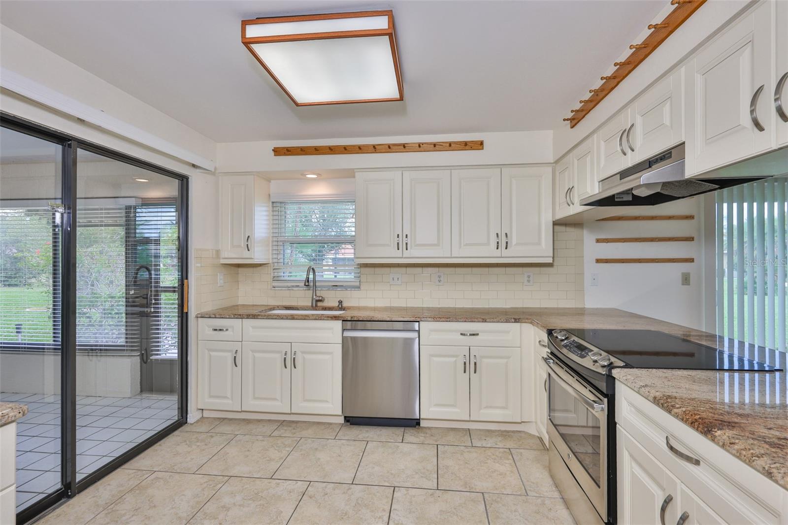 Chef's kitchen, sliders to Florida Room, stainless dishwasher, stainless smoothtop range, stainless exhaust hood, tiled backsplash; dinette to right behind breakfast bar and garden view.