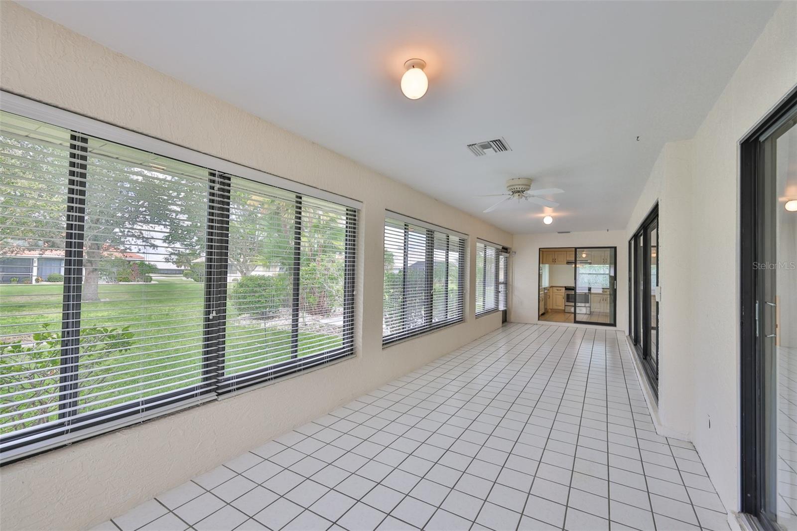 Florida Room - primary bedroom sliders immediate right, far right disappearing slider wall to living room and far center, sliders to kitchen, left garden and far left, door to patio with awning and garden.