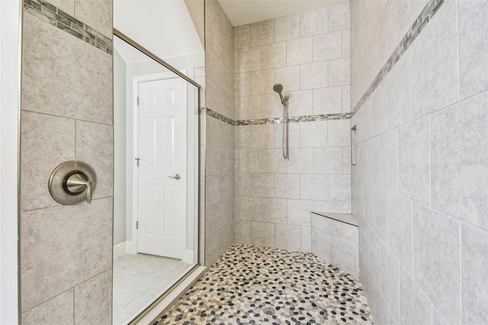 Relax in this walk-in tiled shower with bench and pebble flooring.