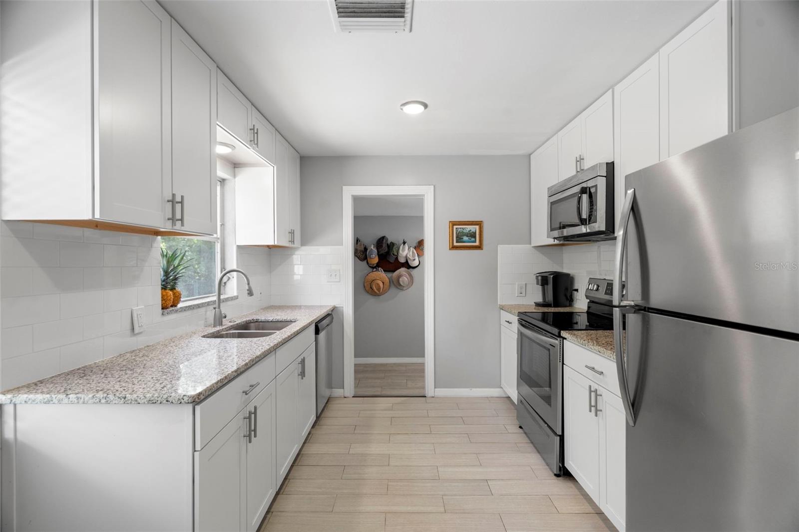 Extended white shaker style cabinetry, stone countertops, a subway tile backsplash, stainless steel appliances.