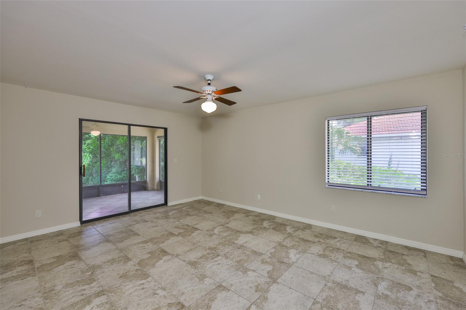 The large primary bedroom has uniform tile floors, sliding glass doors, window fixtures, ceiling fan, and a secluded view.