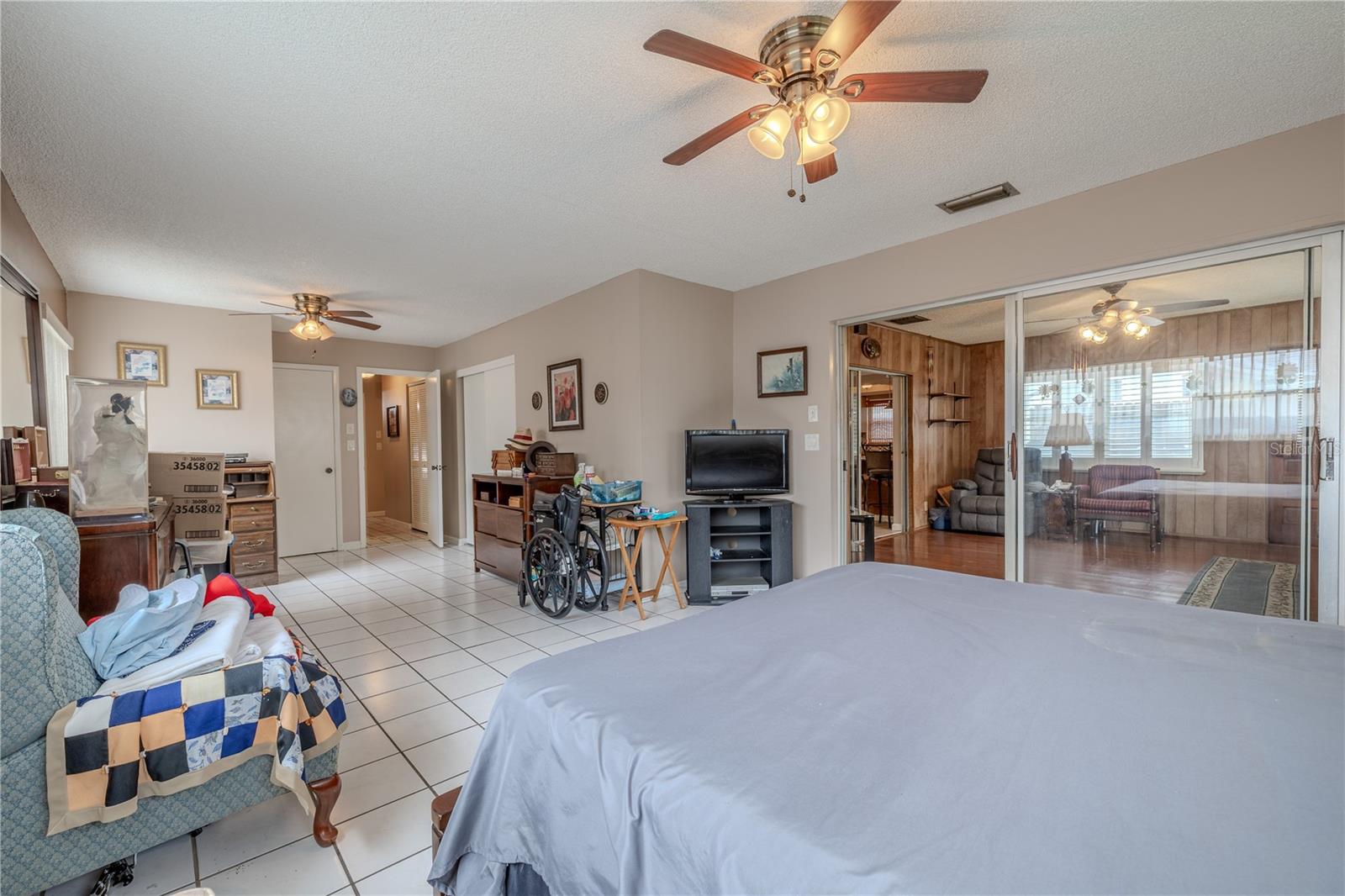 Spacious primary bedroom with tile flooring, dual ceiling fans, and sliding glass doors that open to the Florida room. The room offers ample space for a sitting area or additional furnishings, with direct access to an updated primary bathroom featuring two entry points—one from the bedroom and one from the hallway—for added convenience.