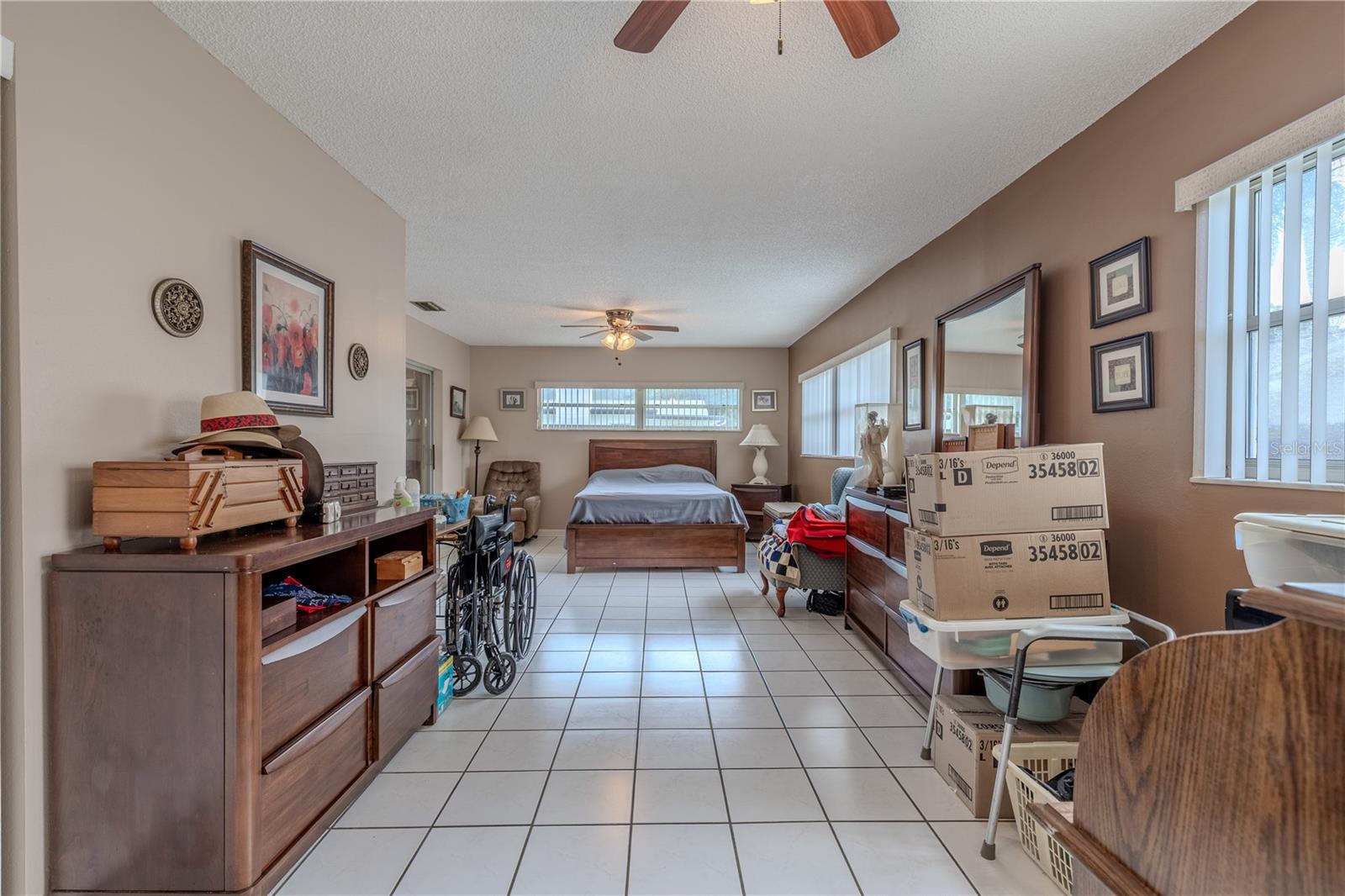 Expansive primary bedroom with tile flooring, neutral wall colors, and dual ceiling fans for comfort. Multiple windows provide abundant natural light, while the generous floor plan allows for a dedicated sitting area or additional furnishings.