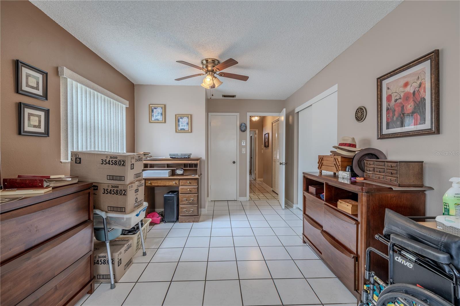 Primary bedroom offers a spacious layout with tile flooring, neutral walls, and a ceiling fan for comfort. Multiple closets provide ample storage, and the room flows easily to the hallway and updated en-suite bathroom. Large windows fill the space with natural light, creating a bright and welcoming retreat.