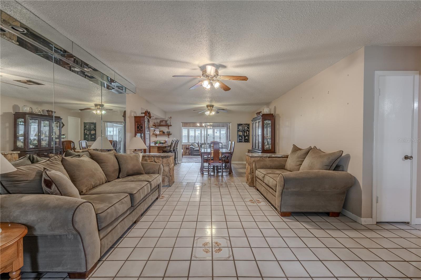 Spacious living room with an open-concept flow to the dining area, featuring neutral tile flooring with decorative inlays and ample natural light from large rear windows.