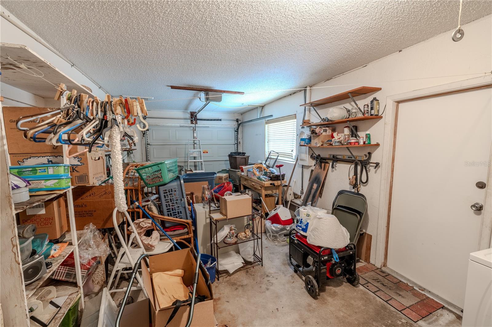 Attached one-car garage with overhead door, side window for natural light, and direct access to the home. Features built-in shelving providing ample storage and workspace options.