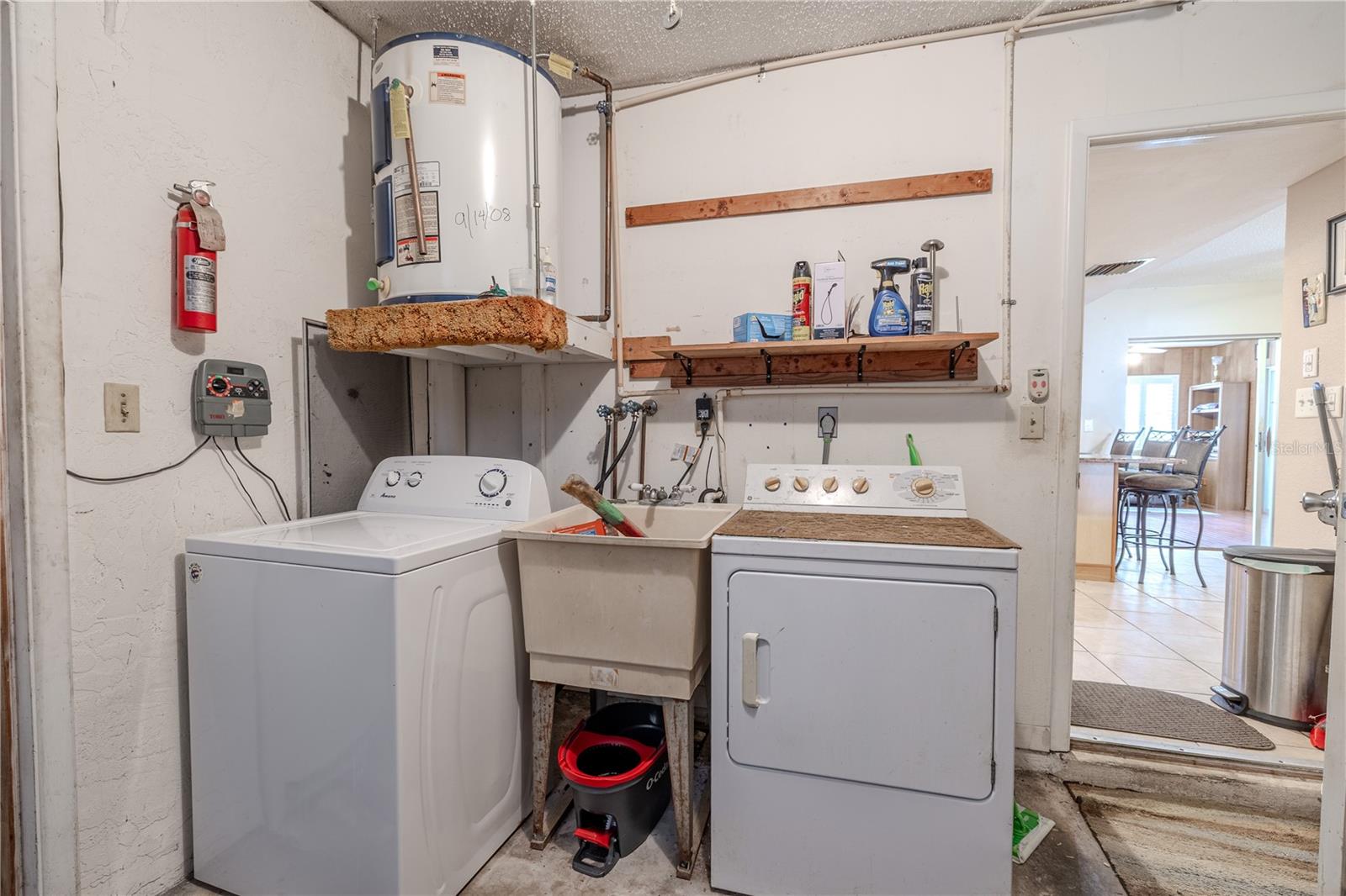 Convenient laundry area located in the garage, featuring a washer, dryer, and deep utility sink. Overhead shelving provides extra storage space for cleaning supplies, while the setup offers easy access from the main living areas.