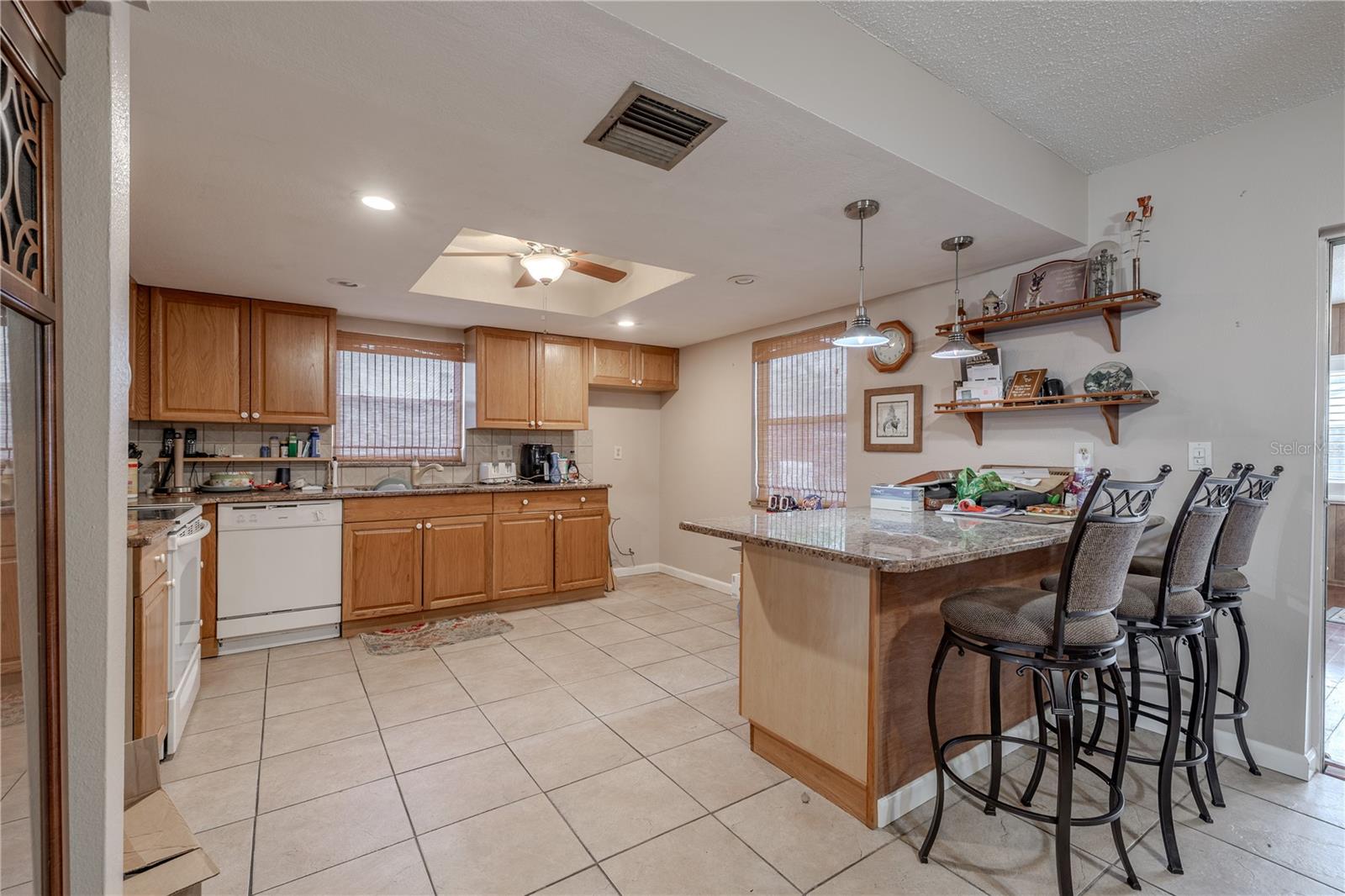 Generously sized kitchen featuring warm wood cabinetry, granite countertops, and a convenient breakfast bar with pendant lighting.Multiple windows bring in abundant natural light, while tile flooring ensures easy maintenance. The open layout flows seamlessly to the dining area, perfect for both everyday meals and entertaining.