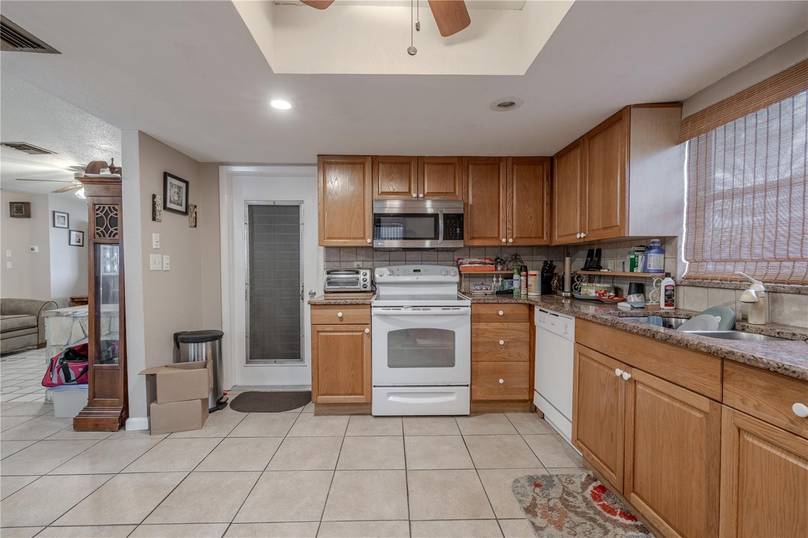 Well-appointed kitchen with abundant wood cabinetry, granite-look countertops, and a tile backsplash. Features include a range, microwave, and dishwasher, along with a window over the sink for added natural light. Convenient access door leads directly to the garage, making grocery trips quick and easy.