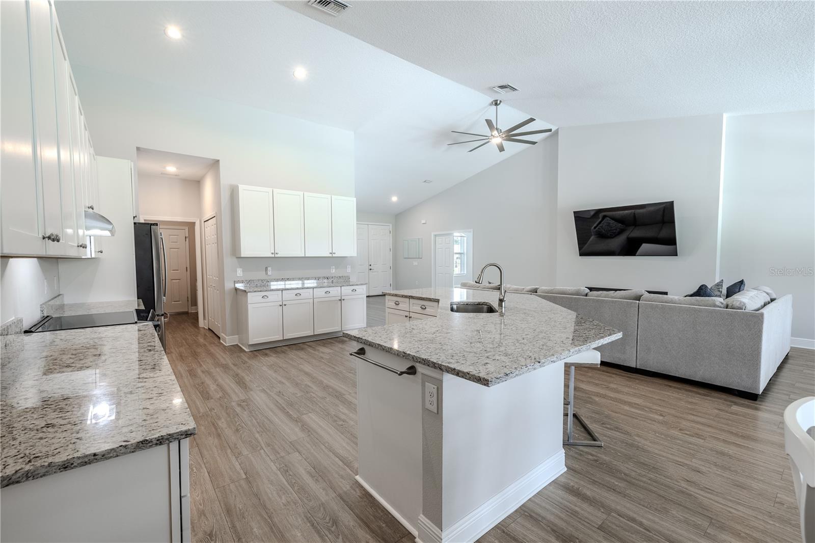 The kitchen’s generous layout and connection to the family room are on full display. A large center island with sink and breakfast bar seating anchors the space, complemented by expansive granite countertops and abundant white cabinetry for storage.