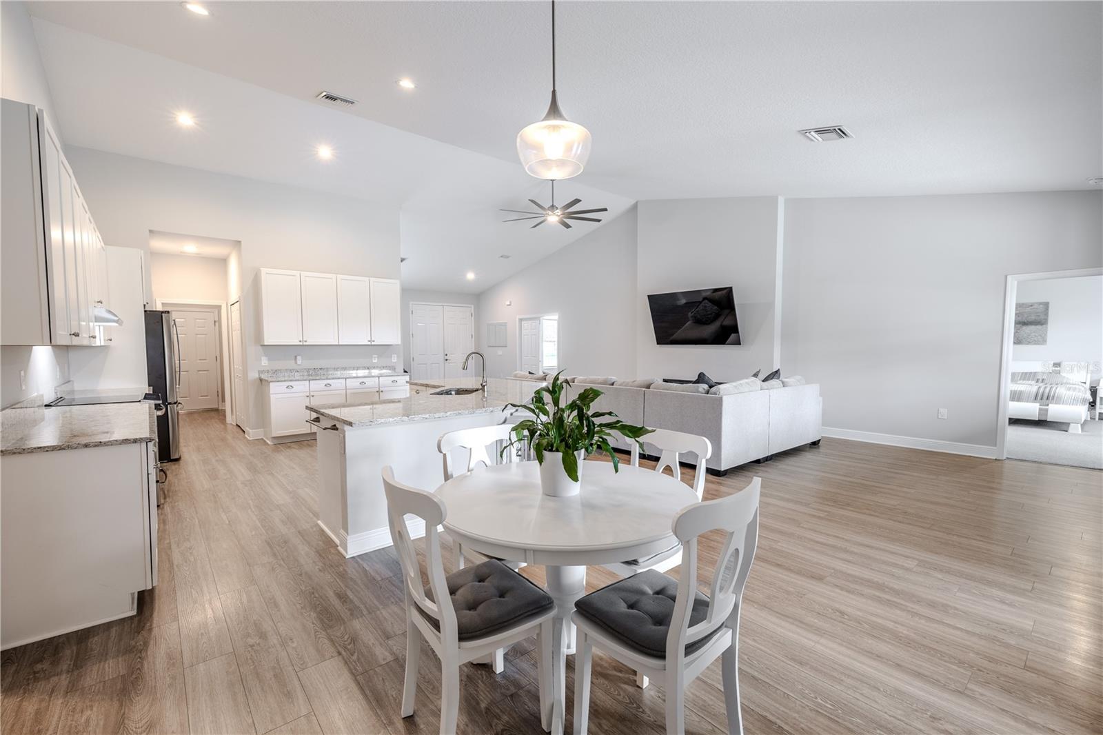 The dining area is bright and welcoming, featuring wood-look flooring, neutral tones, and a modern pendant light fixture. Open to both the kitchen and family room, this space offers seamless flow for everyday living and entertaining. Its central location allows easy conversation and connection while enjoying meals, with open sightlines to the main living spaces.