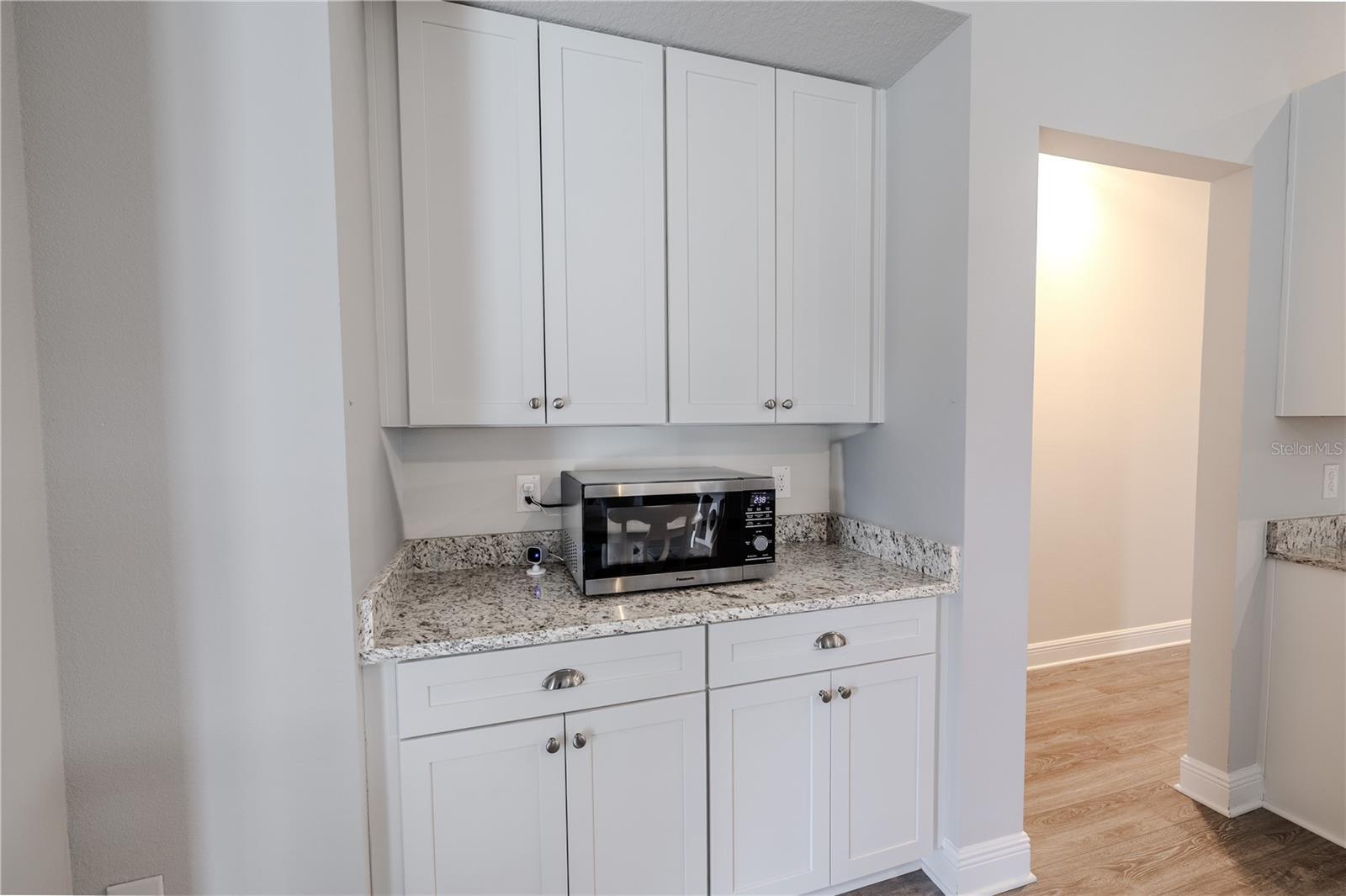 Built-in cabinetry offers additional storage and serving space, featuring crisp white shaker-style doors, brushed nickel hardware, and a coordinating granite countertop with matching backsplash. This versatile area is perfect for use as a buffet, coffee station, or display area, adding both style and functionality to the dining space.