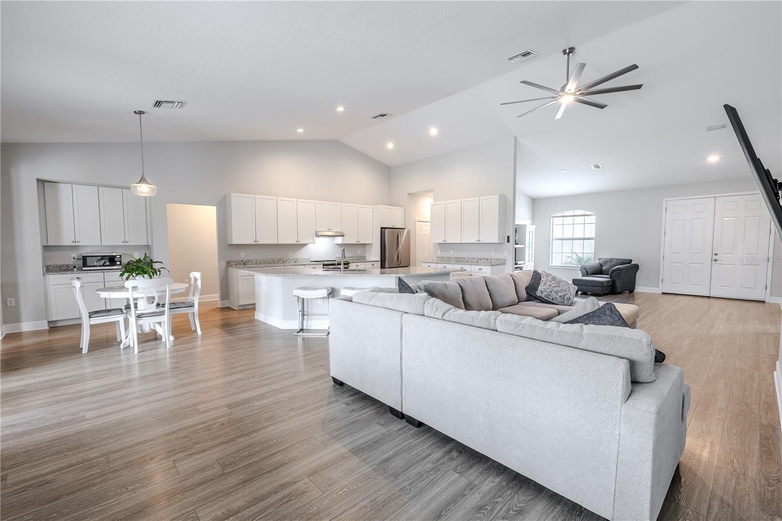 The heart of the home is an expansive open-concept space seamlessly connecting the kitchen, dining area, and family room. High ceilings, recessed lighting, and wood-look flooring enhance the bright, airy feel, while a large sectional seating area offers plenty of room for gatherings.