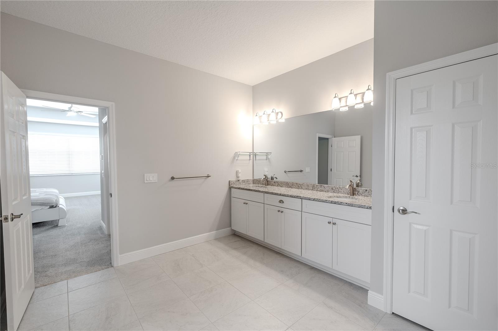The primary bathroom features a spacious double vanity with granite countertops, undermount sinks, and ample storage in white cabinetry.
