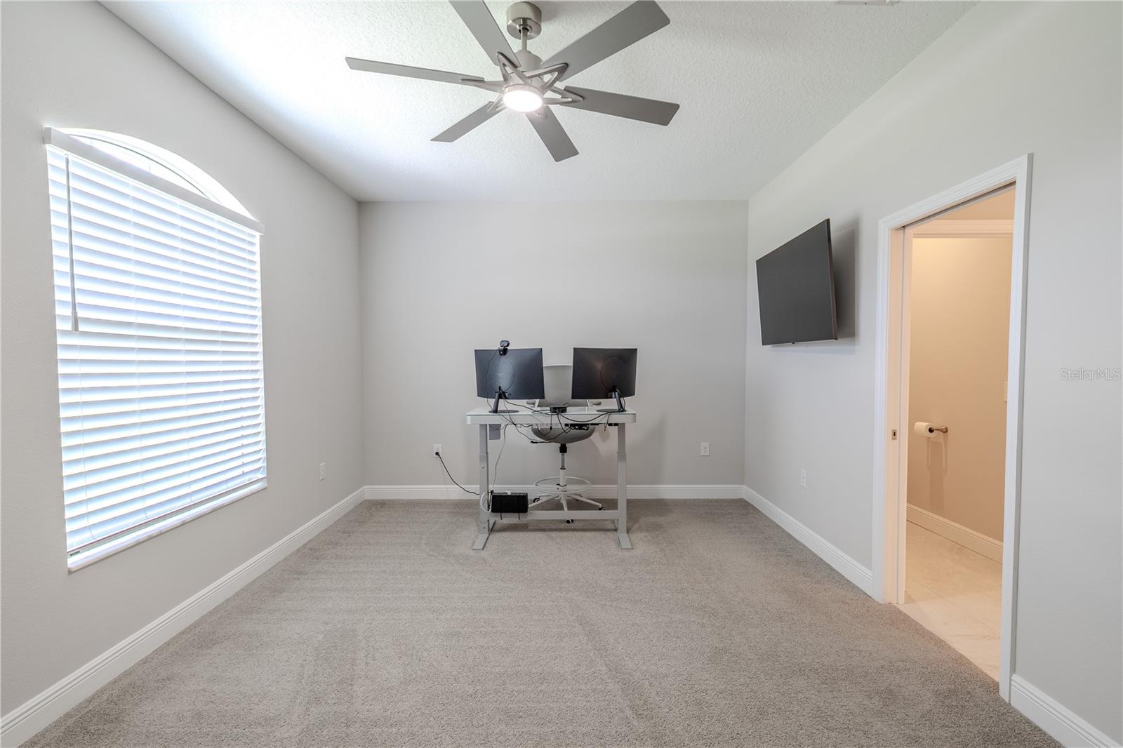 Currently arranged as a home office, this bright and neutral carpeted room offers endless possibilities. With its spacious layout, large arched window, and direct access to a Jack-and-Jill bathroom, it could easily be transformed into a serene nursery, a comfortable sitting room, or a welcoming guest bedroom. The soft natural light makes it equally suited for a craft or hobby space, while its proximity to the primary suite adds convenience for a reading nook or private retreat.