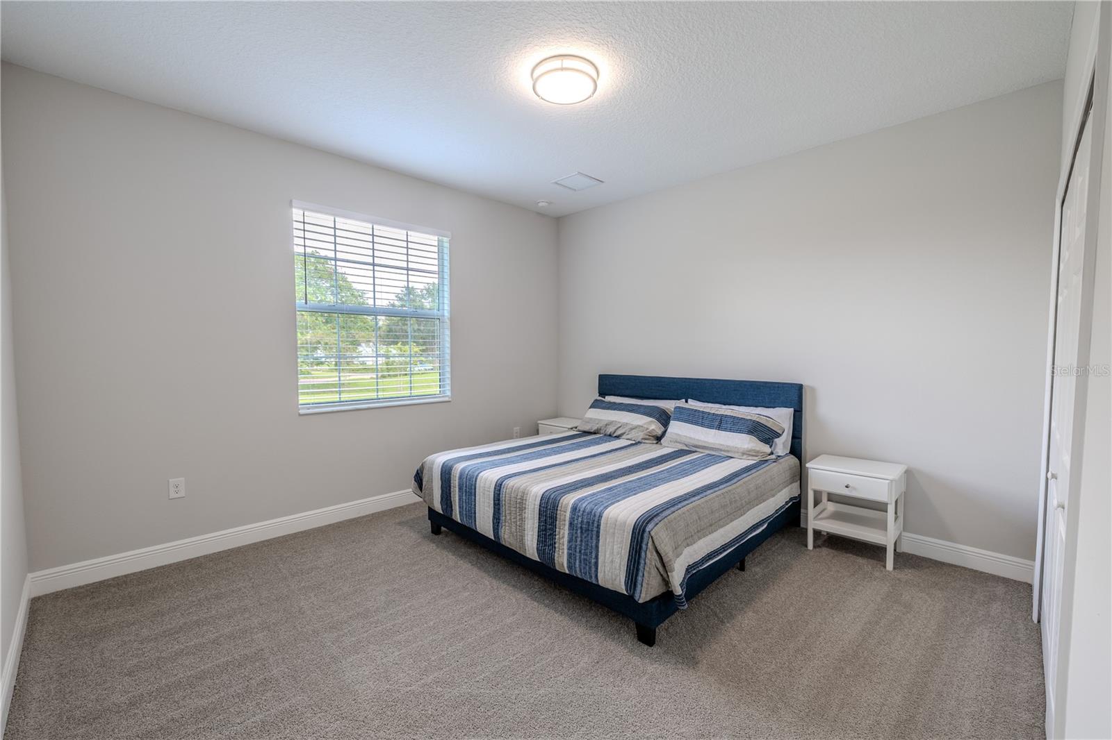 The third bedroom is bright and welcoming, featuring a large window that brings in abundant natural light and highlights  views of the greenery outside. Soft, neutral-toned carpet covers the floor, creating a cozy and comfortable feel.