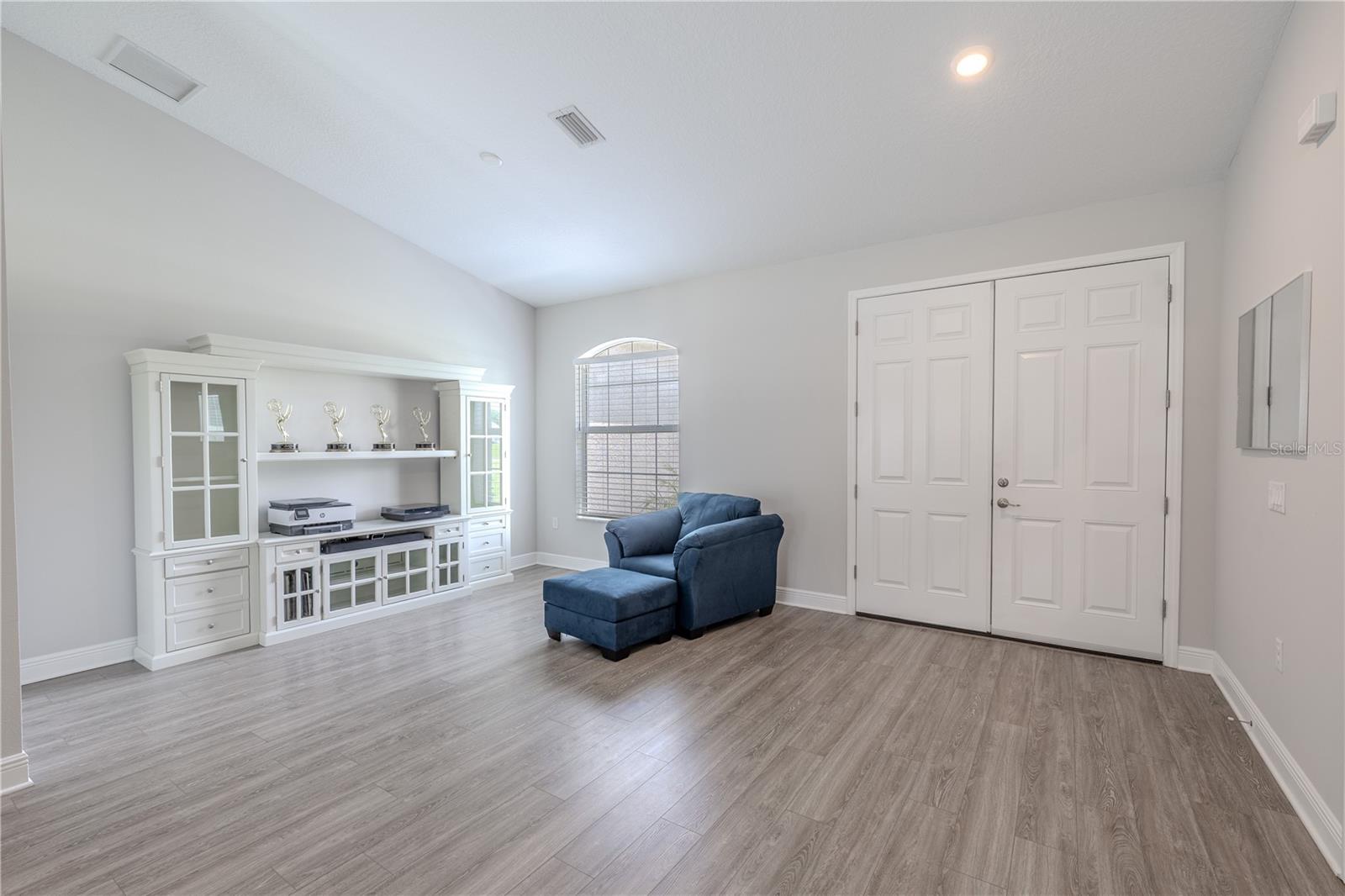 Bright and welcoming, the living room features soaring ceilings, soft neutral wall tones, and wide-plank wood-look flooring that adds warmth and style. A large arched window fills the space with natural light, while the open layout offers flexibility for seating and entertaining. The double-door entry creates an impressive first impression, and the room’s generous proportions make it ideal for both formal and casual gatherings.