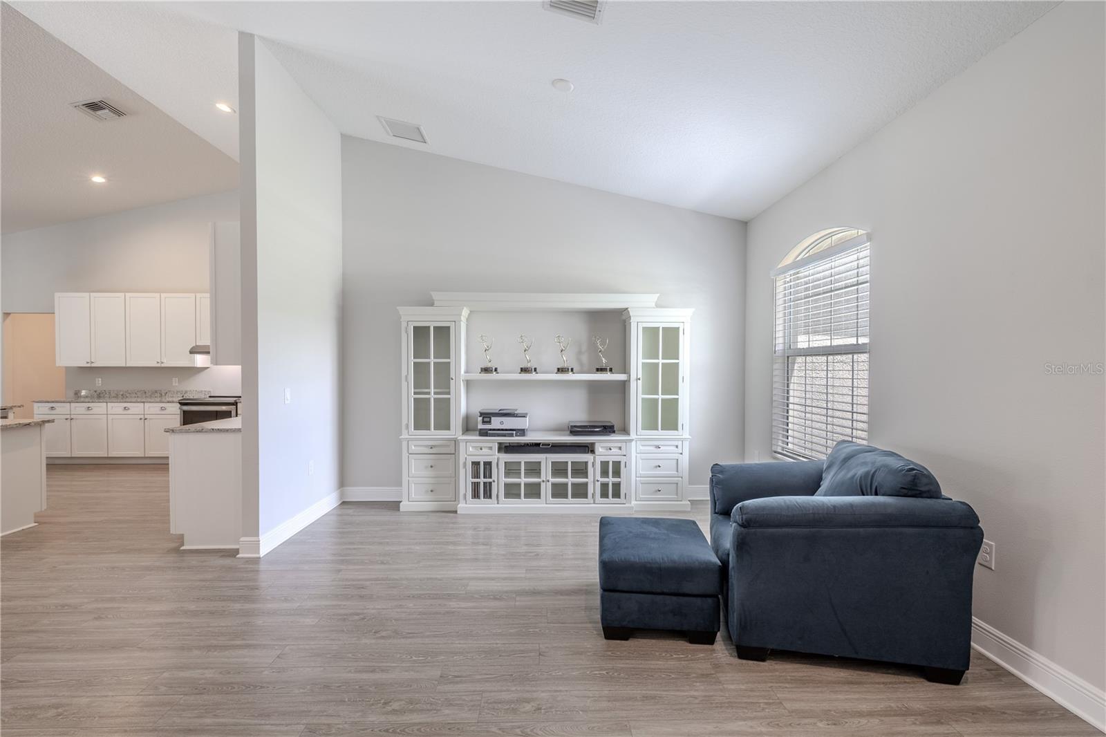 This bright living space flows seamlessly into the kitchen, creating an open and inviting atmosphere. Neutral walls and wide-plank wood-look flooring enhance the modern appeal, while a large arched window allows natural light to pour in. The layout offers versatility for both relaxation and entertaining, with easy access to the heart of the home.
